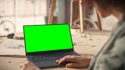 Over the Shoulder Shot of a Furniture Designer Working on Laptop Computer with Green Screen Mock Up...