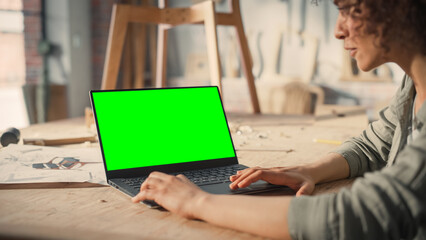 Multiethnic Furniture Designer Working on Laptop Computer with Green Screen Mock Up Display. Creative Female Preparing a Design for Carpentry Project.