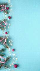 Christmas garland, border, banner with fir twigs, candy canes, garland, and red trinkets. Top view, flat lay, festive Xmas background on mint blue. Wallpaper for social media stories with copy-space.