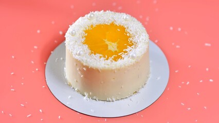 Cake with orange and coconut shavings spun on a pink background.