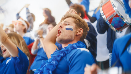 Sport Stadium Big Event: Handsome Happy Caucasian Man Emotionally Cheers, Screams. Crowd of Fans with Painted Faces Celebrate Championship Victor, their Blue Soccer Team is Winning.