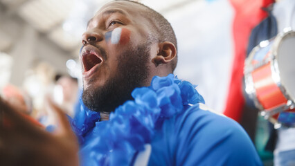 Obraz premium Sport Stadium Big Event: Handsome Black Man Cheering. Crowd of Fans with Painted Faces Shout for their Blue Soccer Team to Win. People Celebrate Scoring a Goal, Championship Victory.