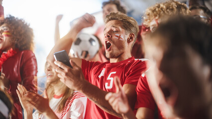 Sport Stadium Soccer Match: Caucasian Man Using Smartphone Cheering for Red Team to Win, Looking at...