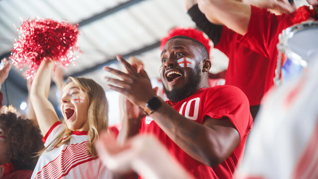 Sport Stadium Sport Event: Close-up Portrait of Handsome Black Man with Painted Cheering for Red Team to Win, Screaming in Celebration of a Victory. International Championship, World Tournament Cup © Gorodenkoff