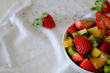 Bowl of healthy fresh fruit salad on a white napkin with strawberries around. Low calories, healthy snack