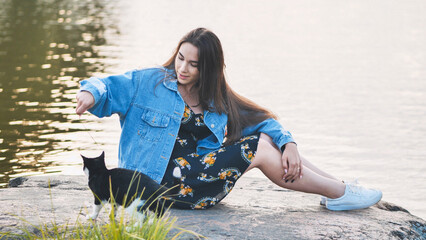 A girl plays with a cat by the lake.