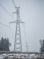 High voltage electricity power line towers near forest at winter. Snow storm.