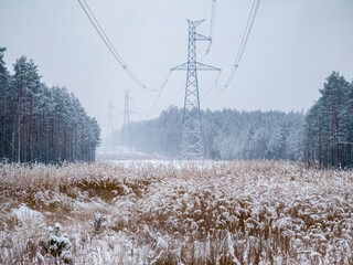 High voltage electricity power line towers near forest at winter. Snow storm.