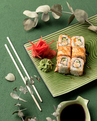 Sushi rolls with baked salmon crab, avocado served on green plate with soy sauce, chopsticks, wasabi and ginger. Japanese kitchen. Healthy diet. Vegetarian dish. Top view. Soft focus.