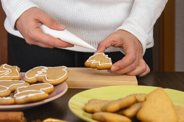 Decorating gingerbread cookies with icing on rustic table with lights. Christmas holiday tradition and advent. Hands decorating baked christmas cookies with sugar frosting. Family time