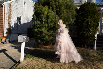 non-binary person wearing pink tulle dress walking across a suburban lawn