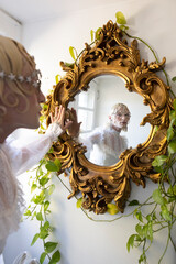 non-binary hispanic person looking at self in ornate gold mirror with mask