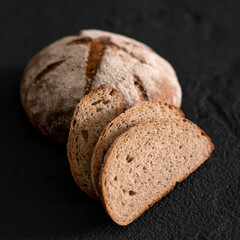 Round loaf of homemade rye bread with cut slices. Traditional family pastry. Fresh bread with crispy crust. Black background. Soft focus. Close-up. Copy space
