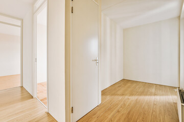 an empty room with white walls and wood flooring on the right, there is a door leading to another...