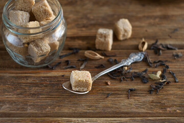 brown sugar in cubes lies on a wooden table. Nearby lies black Indian tea masala