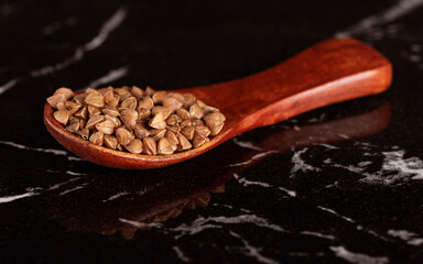 A small wooden spoon with buckwheat on a beautiful marble surface. 
