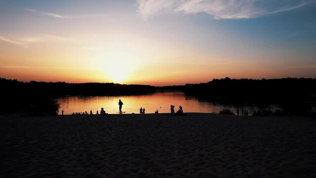 Aerial view of a lake with people relaxing on theon the white sand beach and driveway with parking at sunset