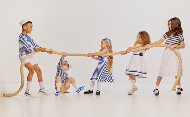 Portrait of children posing in sea style clothes, pulling rope, playing over grey background