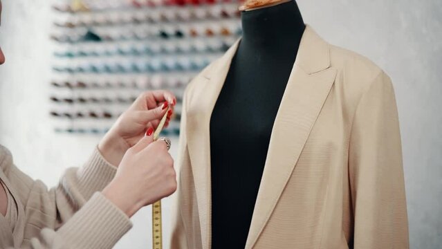 Clothing designer works in the workshop. A woman seamstress takes measurements on a mannequin with a tape.