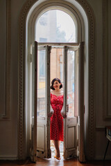 a beautiful and happy brunette women in red retro dress in the balcony doorway 