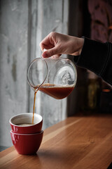 Black coffee is pouring into a cup from glass teapot