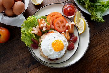 Fried rice and hot dogs, cooked fried eggs, Chinese sausages and ketchup on a wooden background.