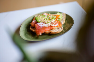 Fresh toast with avocado, salmon, vegan mayonaise, soya sauce and sesame seeds on green plate on marble kitchen top