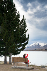Fototapeta na wymiar Asian female tourist pose at turquoise color Lake Tekapo with snow capped New Zealand southern alps at the background. 
