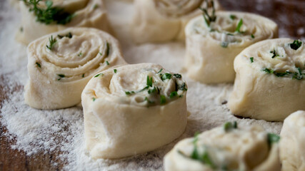 Raw pastry. Dough. The pastry is sprinkled with greens. Dough rolls.
