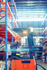 Portrait of a forklift driver wearing a hardhat and vest while moving stock around the floor of a...
