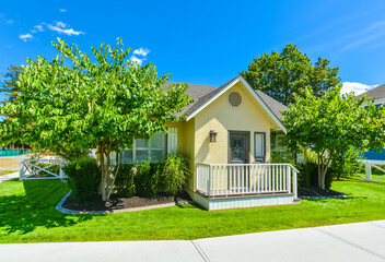 Small yellow family house on sunny day with green lawn and concrete pathway