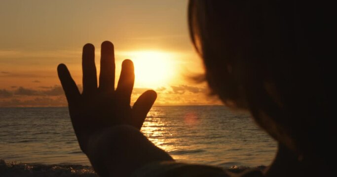 happy little boy dreamer, child catching sunbeams with fingers at sunset, child silhouette by the ocean, happy childhood concept, 4-5 caucasian boy, positive thinking, meditation, human hand