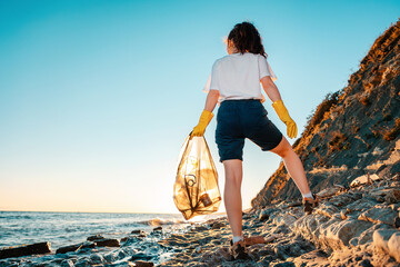A female volunteer stands with a plastic bag in her hand. Back view. Cleaning of the coastal zone...