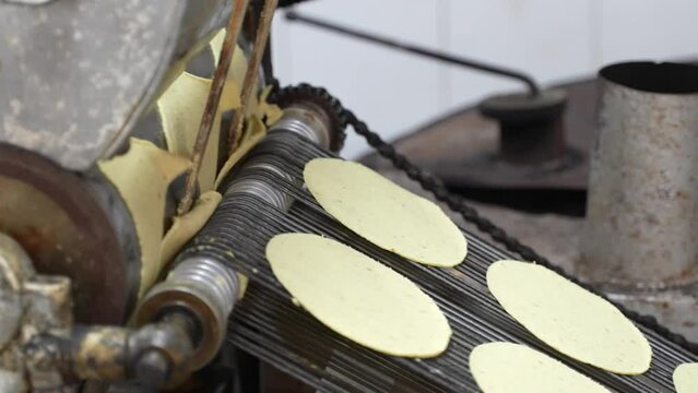 Tortillas stamped out into perfect circles move down a conveyor belt towards the oven where they are cooked.