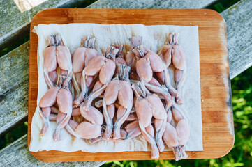 Fresh and juicy frog legs meat on a wooden cutting board, traditional French dish 