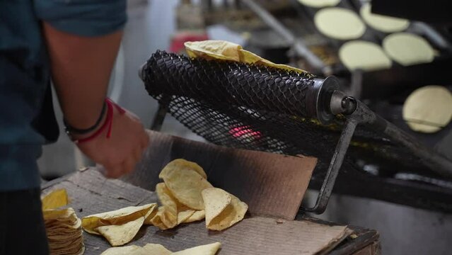 Slow motion closeup of freshly made tortillas flopping off the conveyor belt as a hand picks them and puts them into stacks.
