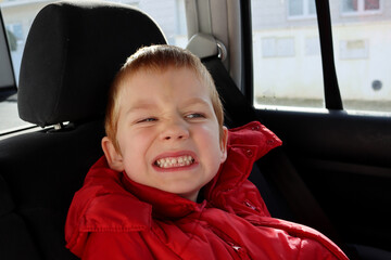 The blond boy wrinkles and grinds his teeth. A cranky five-year-old boy in the cabin of a car. 
