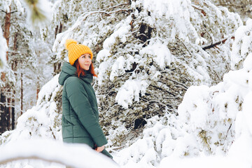 Cheerful girl in warm clothes playing with snow outdoors near the beautiful forest