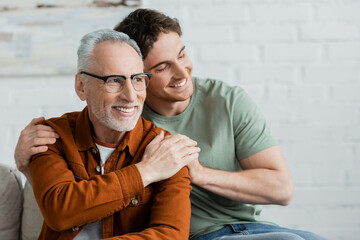 cheerful young man with closed eyes hugging bearded and mature father in eyeglasses