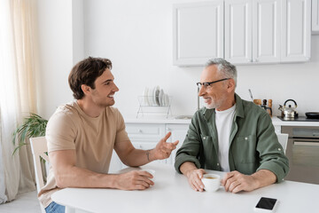 Obraz premium happy young man gesturing while talking with father during breakfast at home