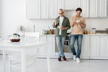 Obraz premium full length of mature father and young son having breakfast while standing in modern kitchen