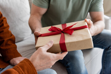 partial view of man holding gift box with red ribbon while congratulating dad on fathers day - Powered by Adobe