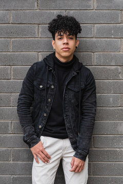 Positive Hispanic migrant guy leaning on brick wall