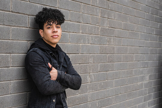 Positive Hispanic migrant guy leaning on brick wall
