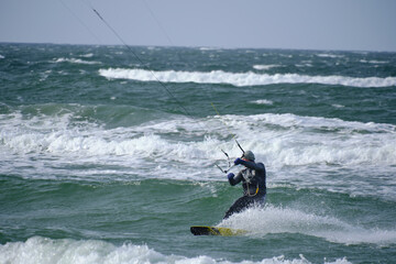 Kitesurfing, riding board waves during storm holding to flying kite.