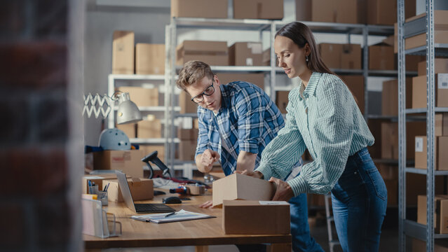 Young Male and Female Warehouse Inventory Managers Packing Orders for Clients, Using Laptop Computer and Checking Retail Stock. Employee Preparing a Parcel with Stylish Retro Bicycle Seat.
