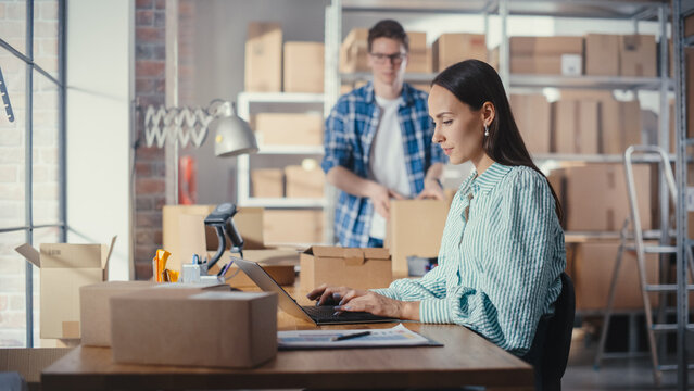 Young Male and Female Warehouse Inventory Managers Packing Orders for Clients, Using Laptop Computer and Checking Retail Stock. Employee Preparing a Parcel with Stylish Retro Bicycle Seat.