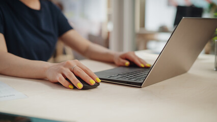Female Employee in Black Casual Clothes Working on Laptop in Office During a Sunny Day. Close Up on Hands with Striking Yellow Nail Polish Typing Texts on a Computer, Writing Emails and Using Mouse.