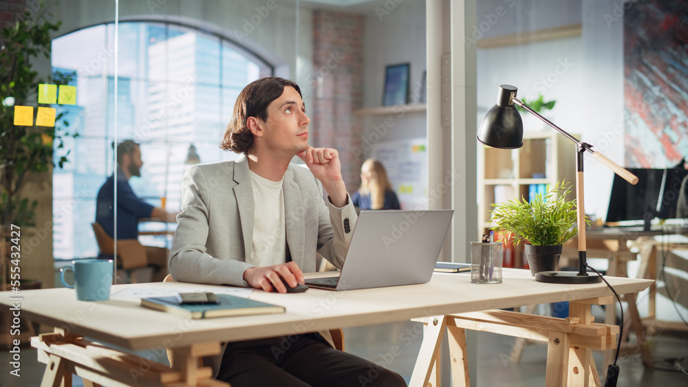 Poster handsome long-haired employee sitting at a desk in creative agency. stylish man using laptop compute