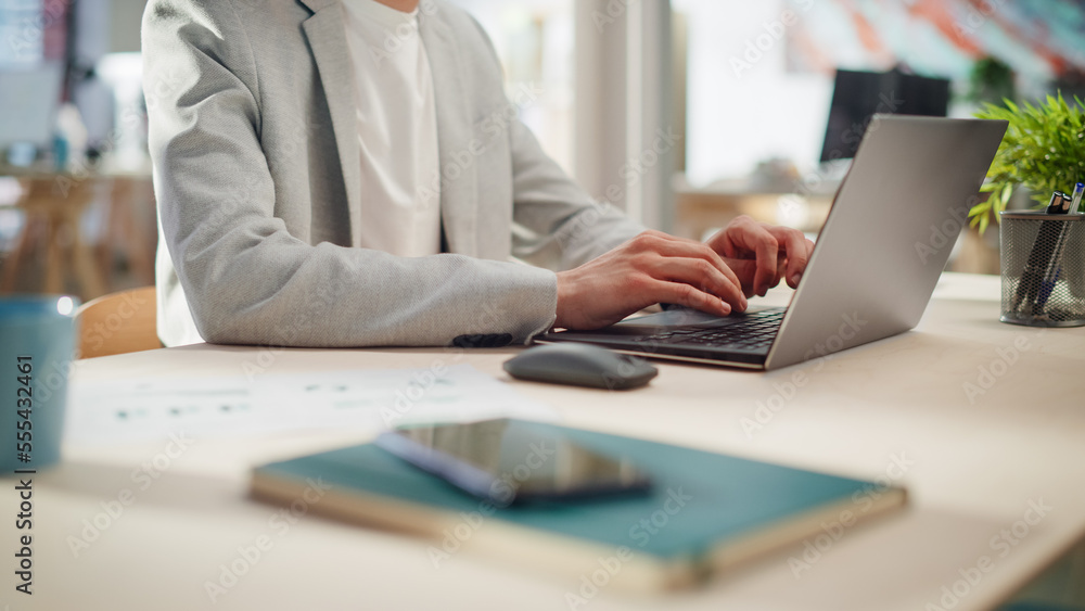 Poster manager sitting at a desk in creative office. focus on hands of a young stylish man in a jacket usin